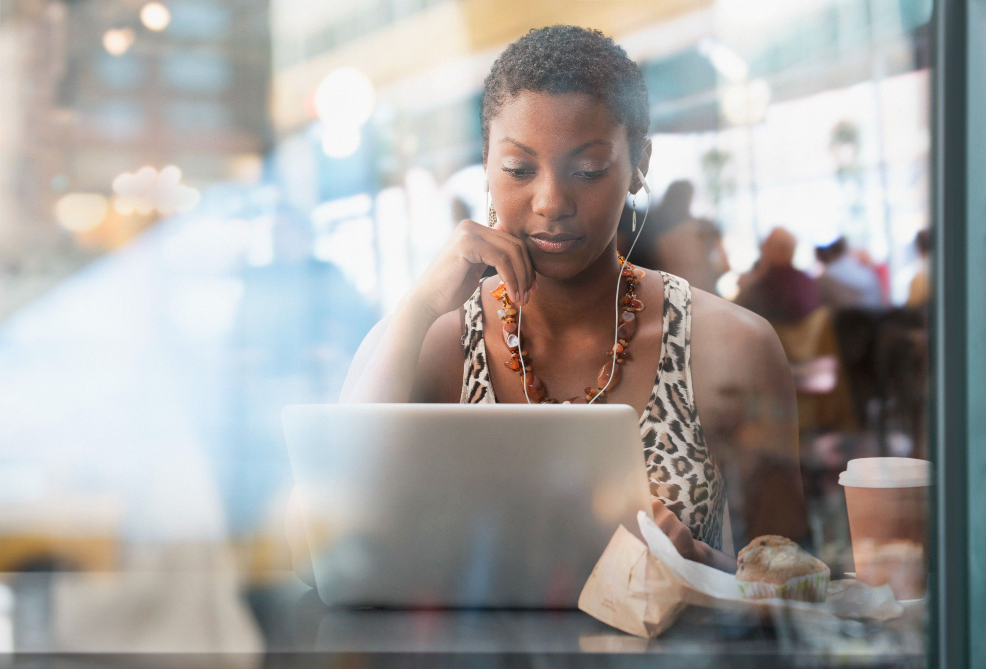 Person focuses on a laptop in a cafe with earbuds in, highlighting how easy it is to split a PDF on a laptop.