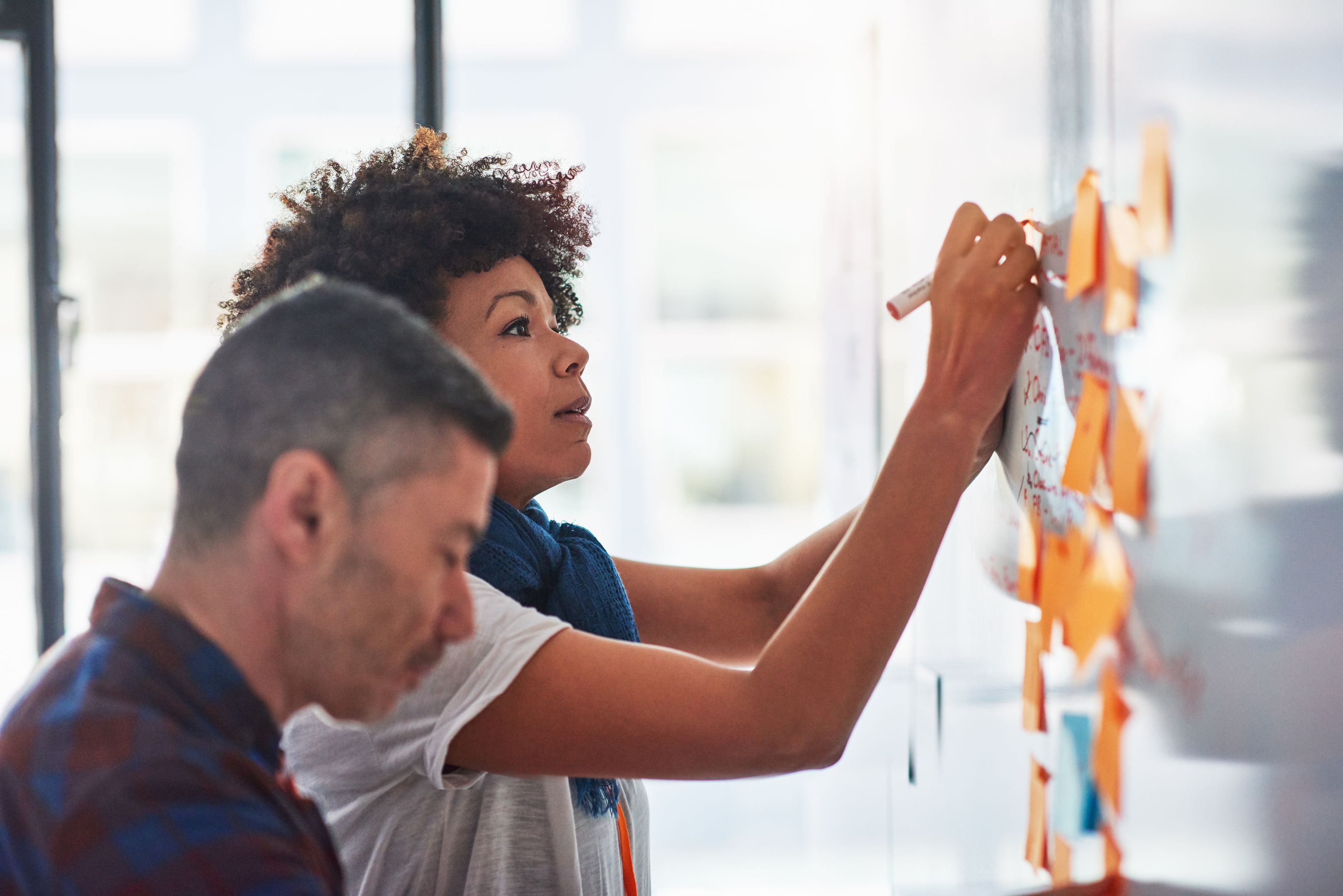 Two people collaborate on workflow management, using a whiteboard and sticky notes to plan tasks and organize ideas.