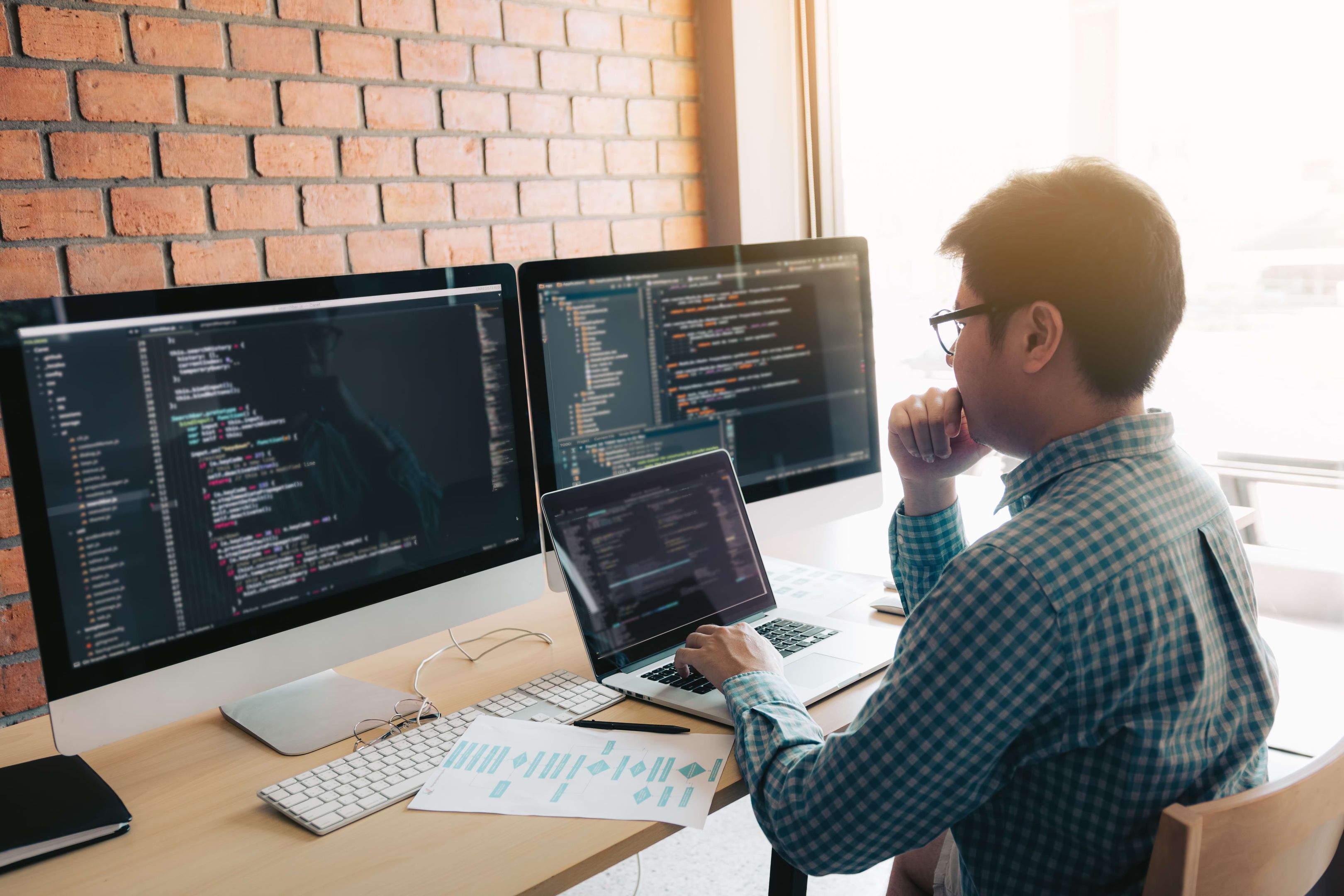 Person reviews code on multiple screens in an office, illustrating the complexity of enterprise data security.