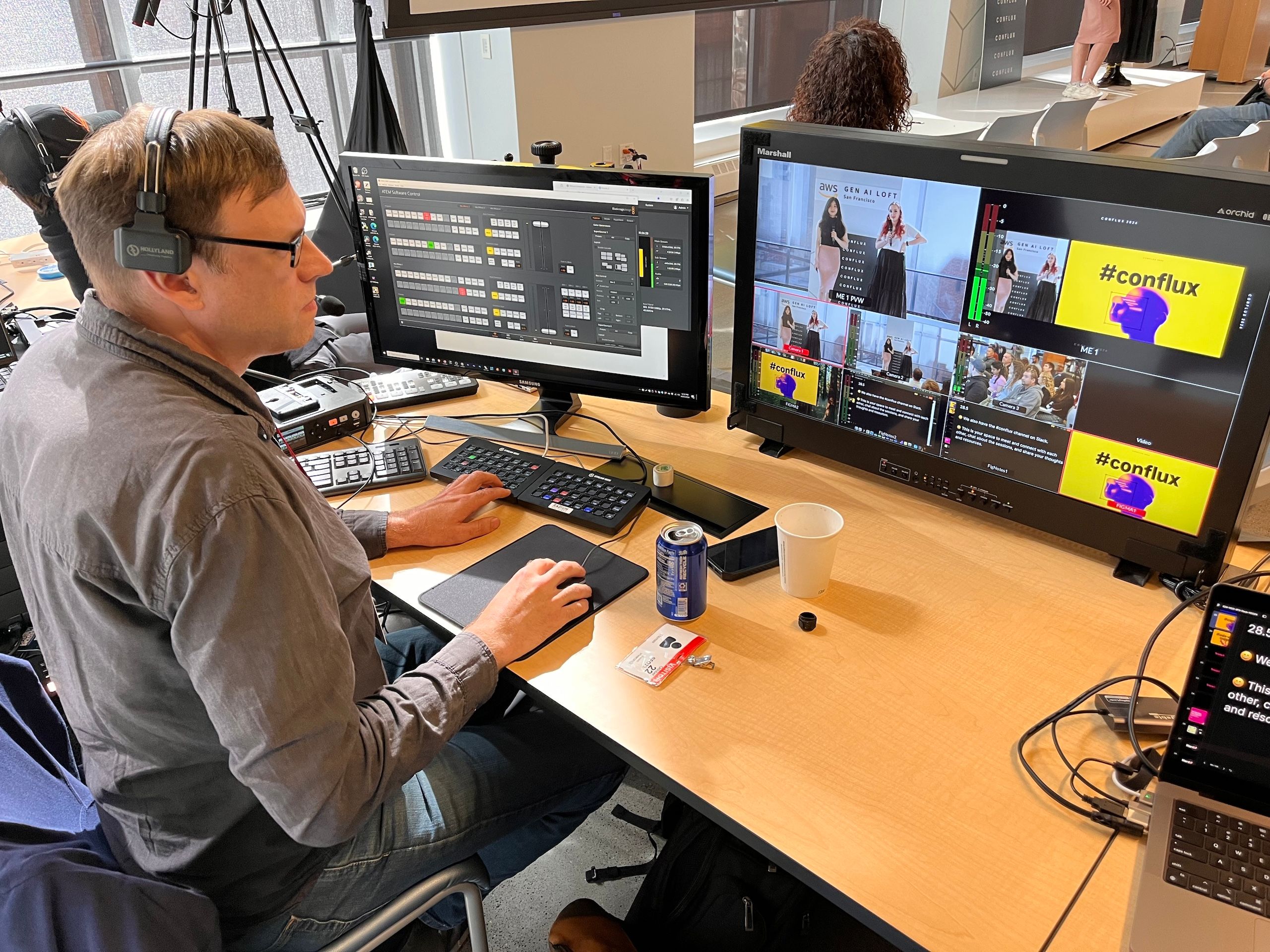 Man with earphones and glasses working with multiple screens at a desk editing video and sound