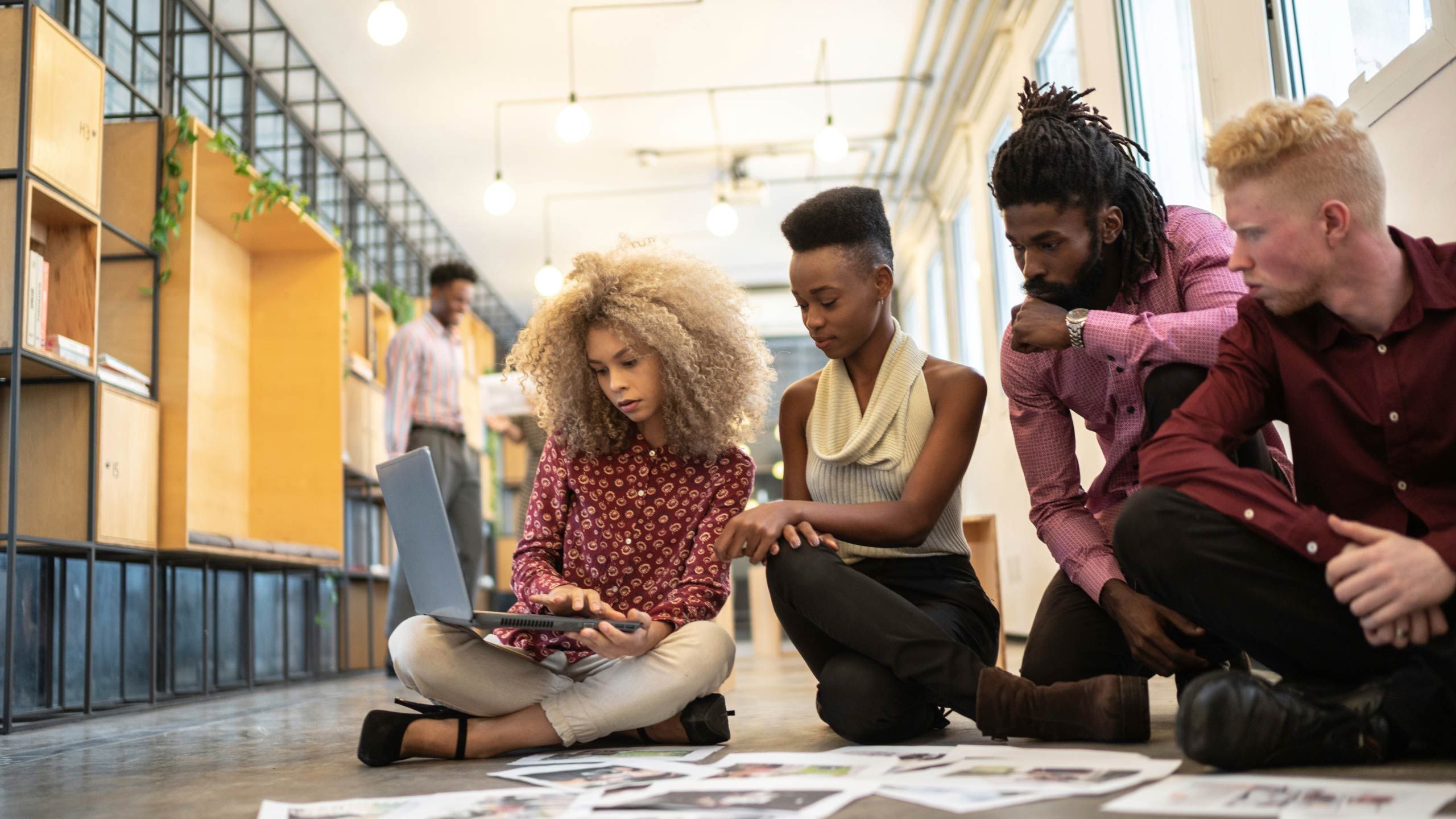 A group of people sitting on the floor looking at a laptop and scattered papers