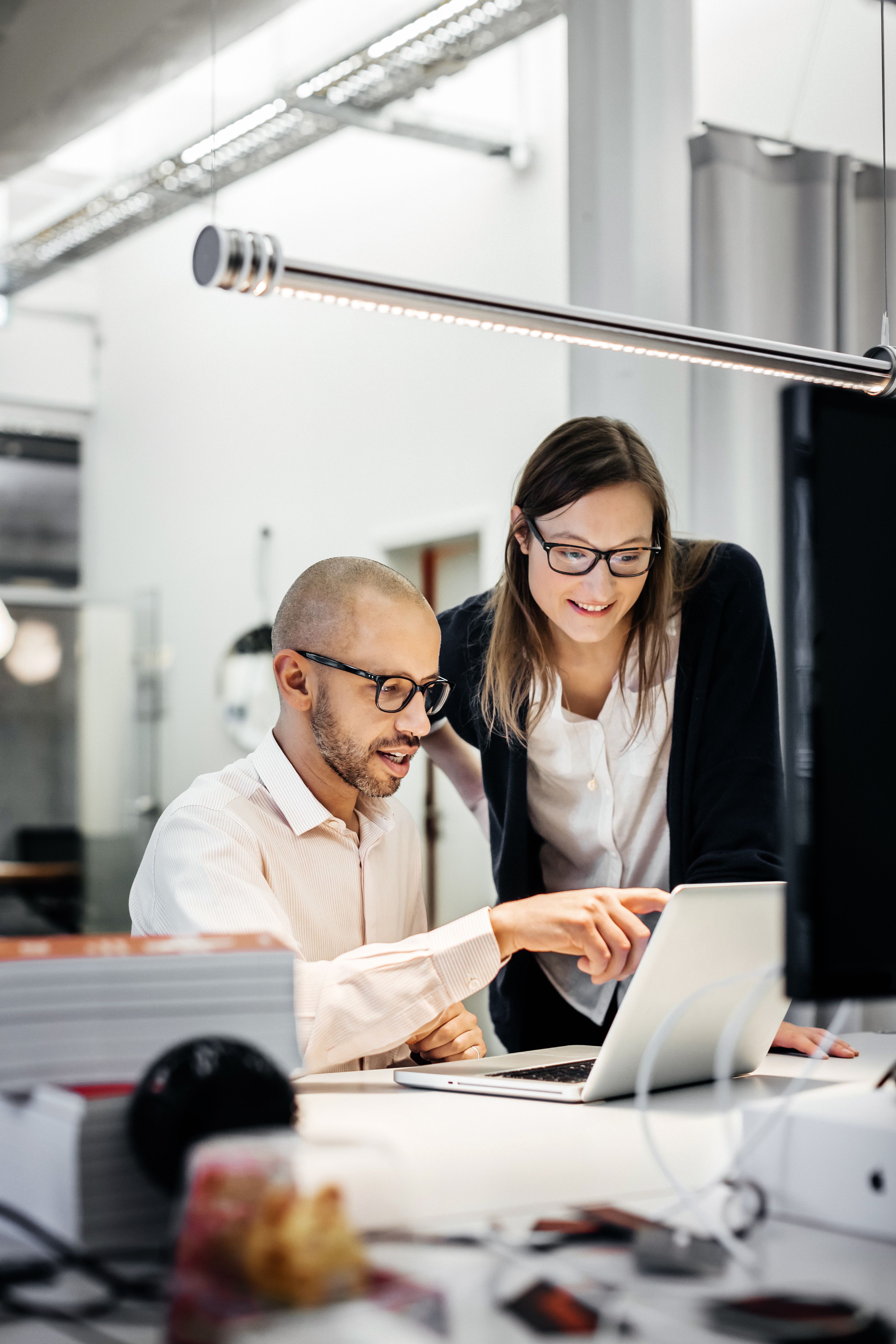 Two people working on a laptop, one person is sitting down and the other is standing beside them.