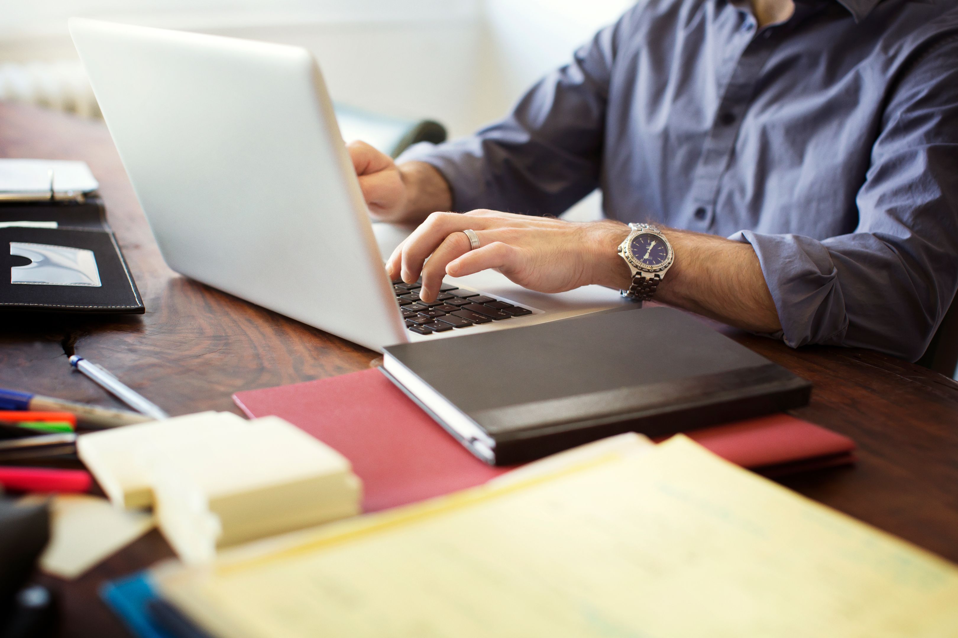 Hands typing on a laptop at a desk with papers and a notebook.
