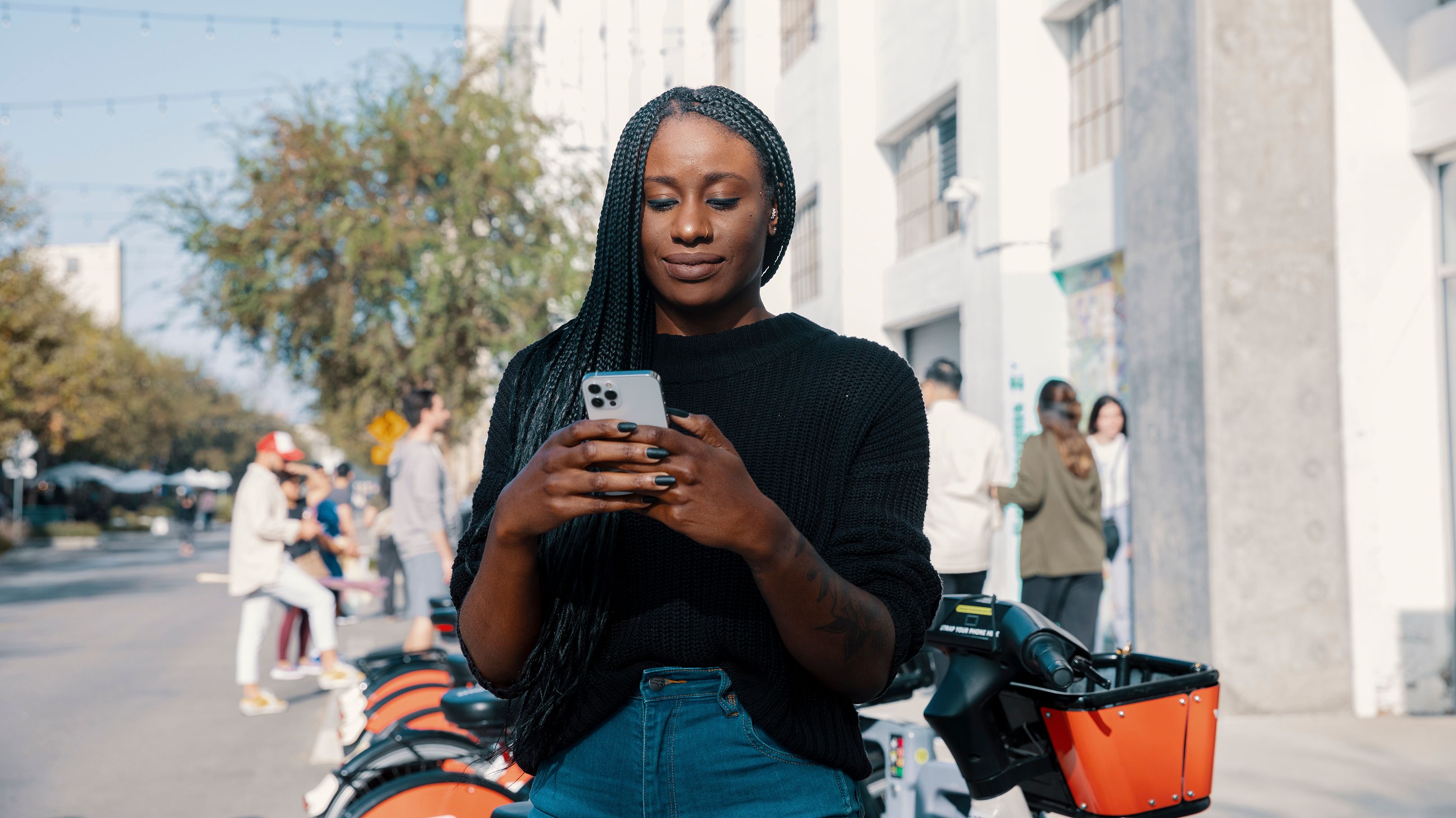 A person standing outdoors on her mobile device in front of a group of people.