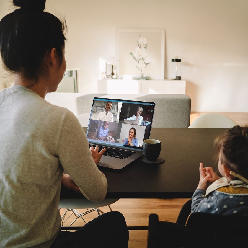A person attends a meeting remotely from their home, while caring for their child.