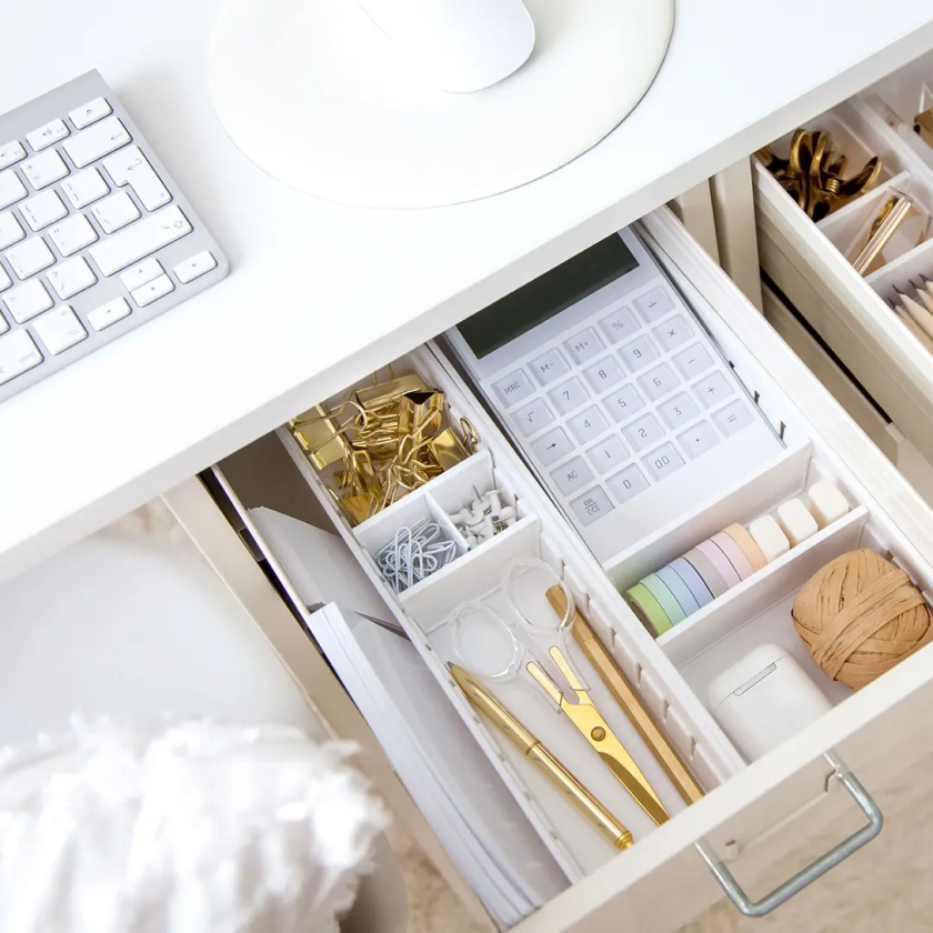 An open drawer in a desk, containing organized compartments full of office supplies and a calculator.