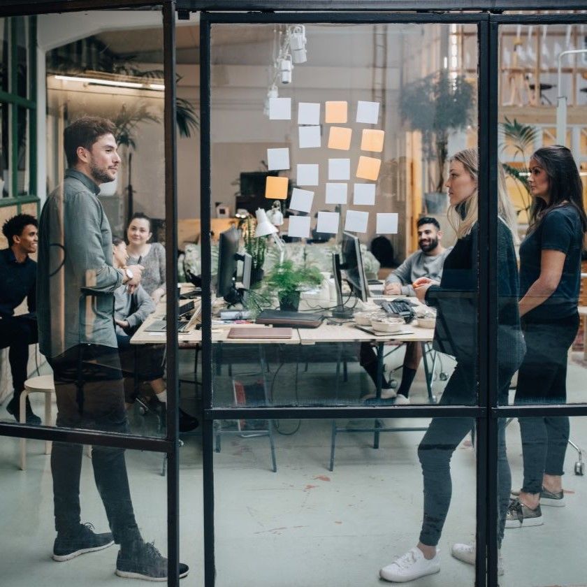 Marketing team gathers in an office space with sticky notes on glass, planning workflows and brainstorming ideas together