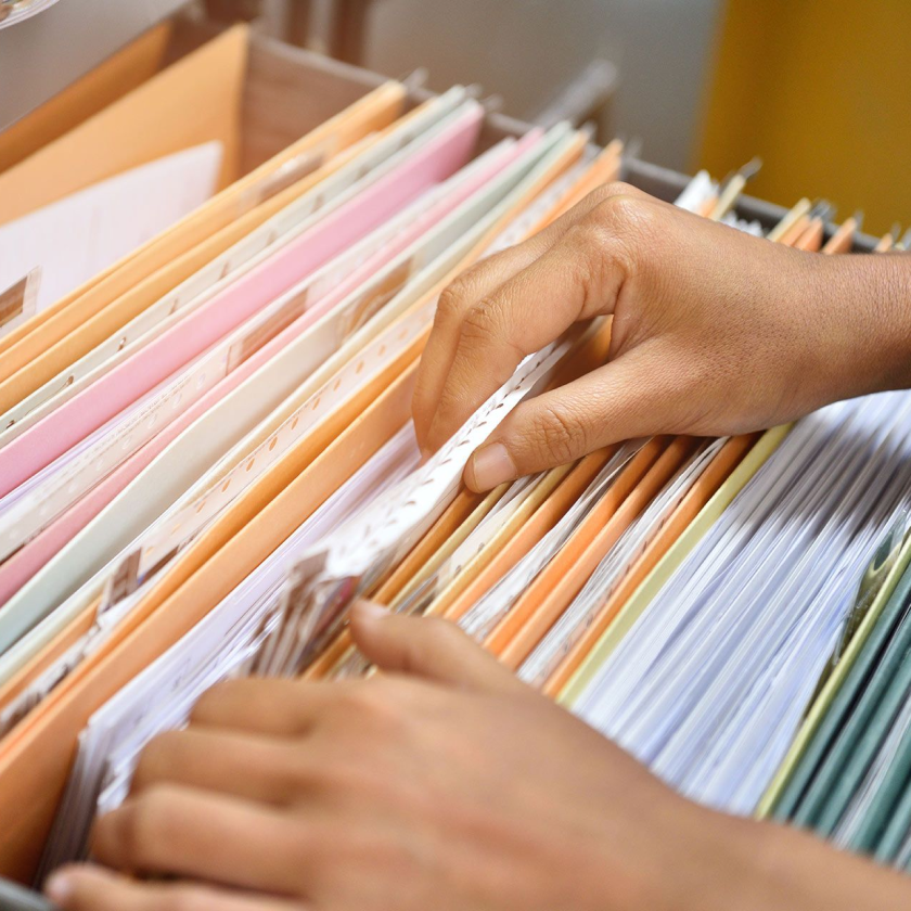 A person uses their hands to sort through a filing cabinet, filled with files and documents.